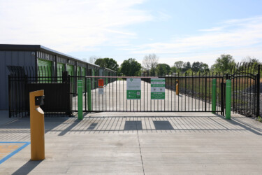 The entrance gate with view of the keypad on yellow pole and indoor storage units during the day